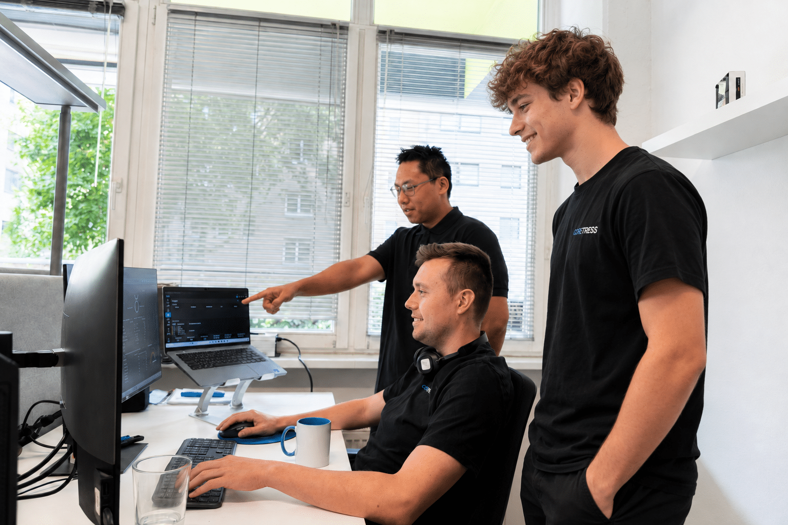 Drei coretress Mitarbeiter arbeiten gemeinsam an einem Computerarbeitsplatz im Büro.